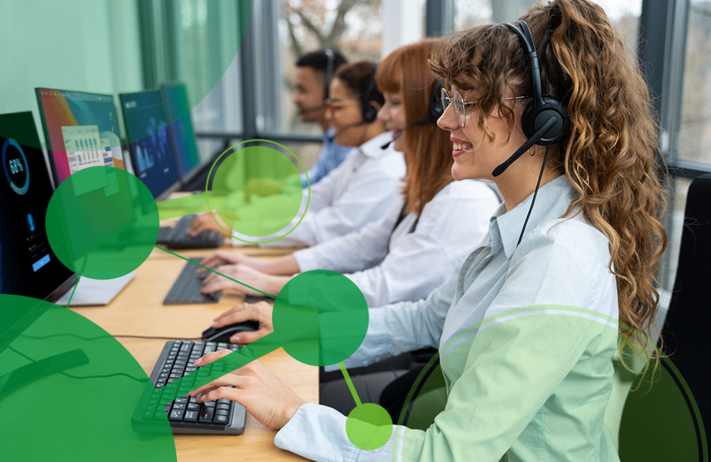 A line of employees sit at their desks on their computers, smiling as they speak into headsets